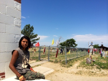 Justin Rowland, a descendant of survivors of the Wounded Knee massacre, sits at the Wounded Knee Memorial. Behind him is a mass grave of those killed. Photo by Elizabeth Hoover